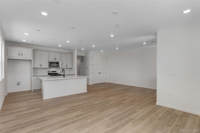 kitchen with appliances with stainless steel finishes, recessed lighting, light wood-style flooring, a center island with sink, and light countertops