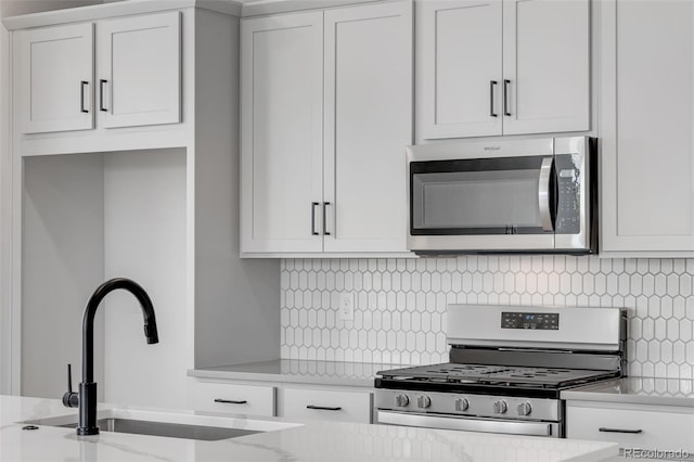kitchen featuring stainless steel appliances, a sink, backsplash, white cabinets, and light stone countertops