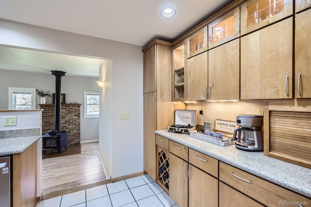 1065 6th St, Berthoud, CO 80513 - kitchen with a wood stove, glass insert cabinets, light tile patterned floors, baseboards, and light stone counters