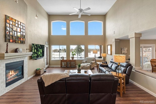 living room with ceiling fan, a fireplace, dark hardwood / wood-style flooring, and decorative columns