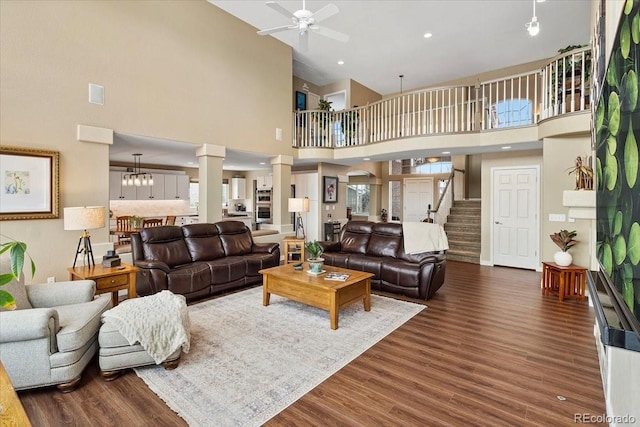 living room featuring dark hardwood / wood-style flooring, a towering ceiling, decorative columns, and ceiling fan