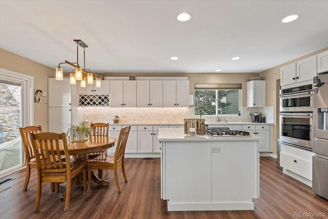 kitchen with appliances with stainless steel finishes, a kitchen island, decorative light fixtures, white cabinets, and backsplash