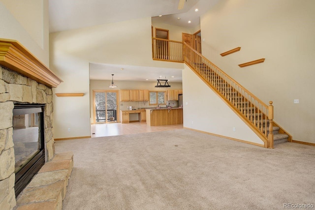 unfurnished living room featuring light carpet, stairway, a fireplace, baseboards, and a towering ceiling