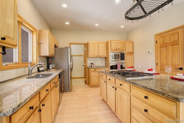 kitchen featuring backsplash, light stone countertops, light brown cabinetry, stainless steel appliances, and a sink