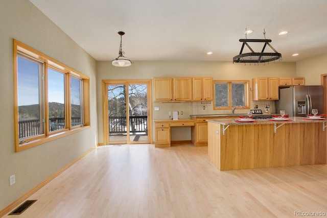 kitchen featuring visible vents, light brown cabinetry, stainless steel refrigerator with ice dispenser, a sink, and a breakfast bar area