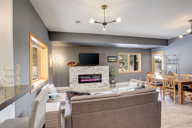 living area with light wood-type flooring, visible vents, a glass covered fireplace, an inviting chandelier, and baseboards