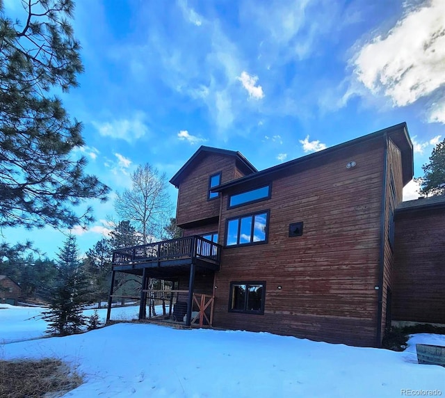 snow covered back of property with a wooden deck