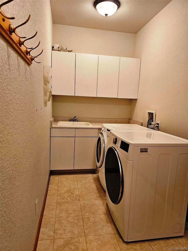 clothes washing area with cabinet space, a sink, a textured ceiling, a textured wall, and independent washer and dryer