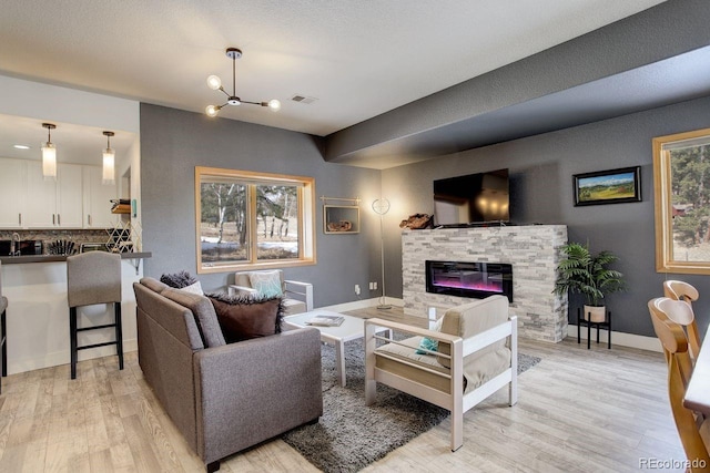 living area with visible vents, baseboards, a fireplace, light wood-style floors, and a notable chandelier