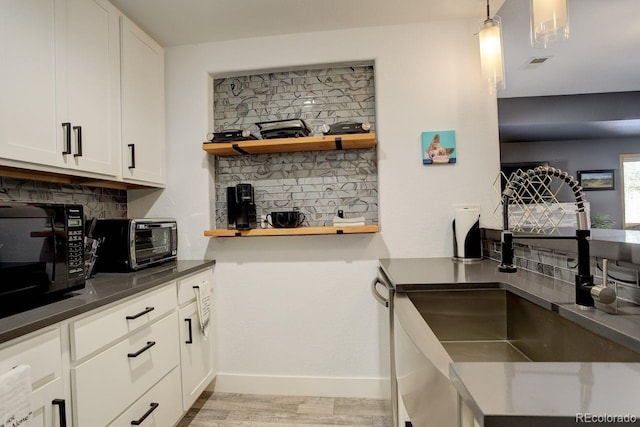 kitchen featuring light wood finished floors, open shelves, white cabinets, black microwave, and dark countertops