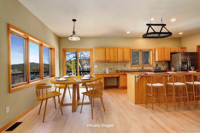 kitchen featuring visible vents, a breakfast bar, a sink, light wood-style floors, and stainless steel refrigerator with ice dispenser