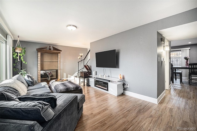 living room with stairs, light wood finished floors, a brick fireplace, and baseboards