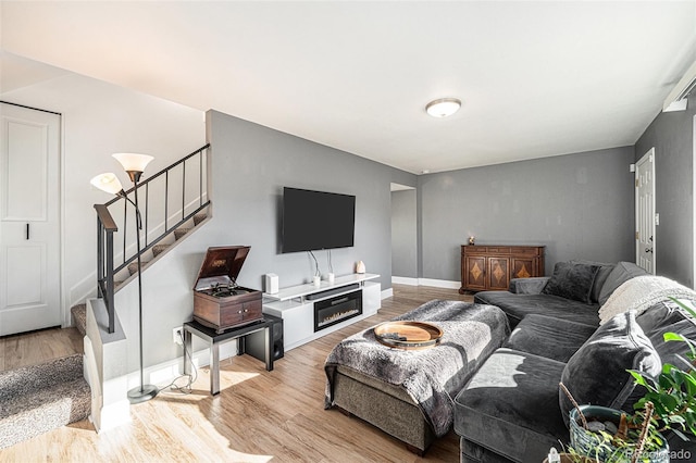 living room featuring light wood-style floors, a fireplace, baseboards, and stairs