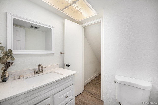 half bath with toilet, vanity, wood finished floors, and visible vents