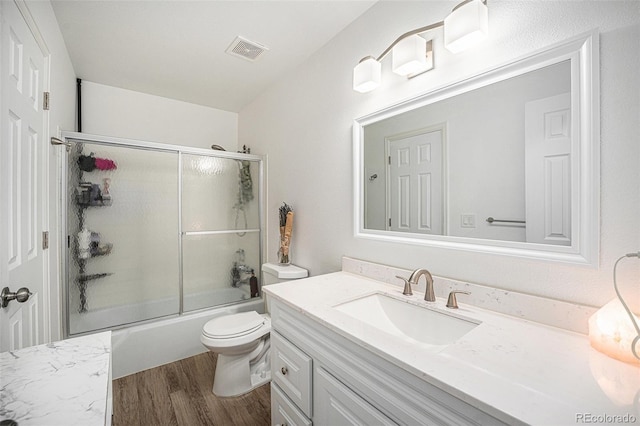 bathroom with visible vents, bath / shower combo with glass door, toilet, wood finished floors, and vanity