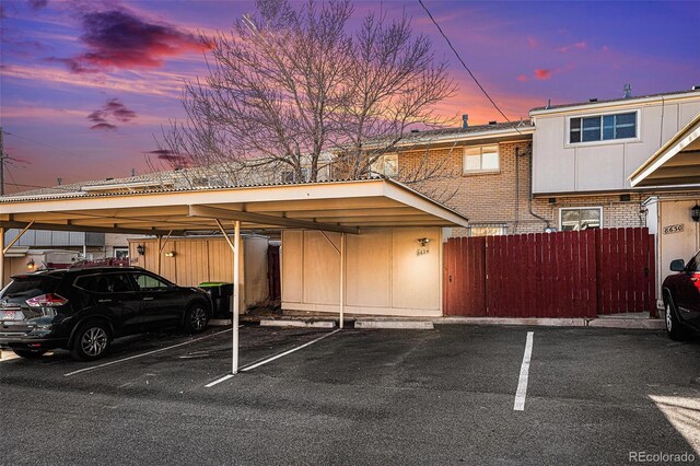 parking at dusk featuring covered and uncovered parking and fence