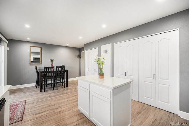 kitchen featuring light wood-style flooring, a kitchen island, baseboards, and white cabinets