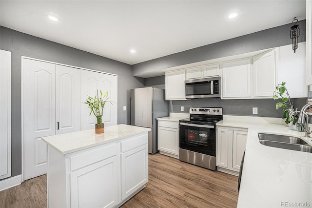 kitchen featuring stainless steel appliances, light wood-style flooring, white cabinetry, a sink, and a kitchen island