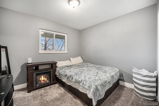 bedroom featuring a warm lit fireplace, baseboards, and carpet flooring