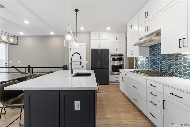 kitchen featuring under cabinet range hood, a sink, appliances with stainless steel finishes, tasteful backsplash, and a kitchen bar