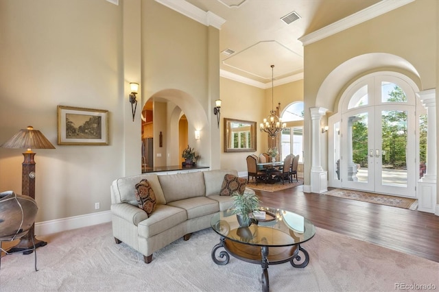 living room featuring french doors, ornamental molding, a towering ceiling, light wood-type flooring, and a chandelier