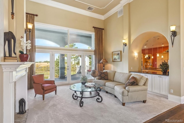 living room with a towering ceiling, light hardwood / wood-style flooring, french doors, and ornamental molding