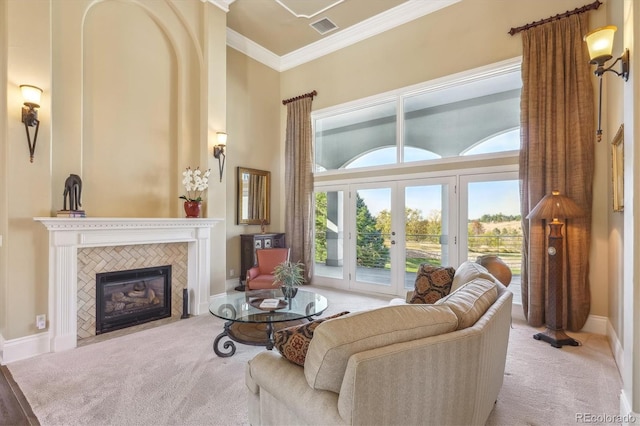 carpeted living room with a towering ceiling, french doors, crown molding, and a tile fireplace