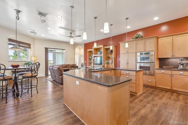 kitchen featuring hardwood / wood-style flooring, decorative light fixtures, an island with sink, and stainless steel double oven