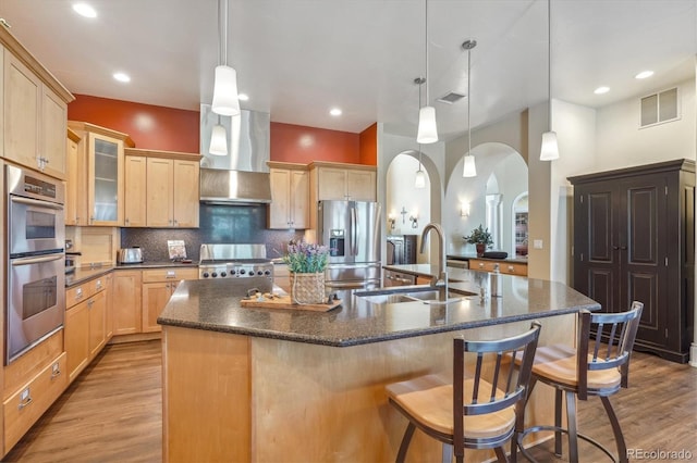 kitchen featuring stainless steel appliances, sink, a kitchen island with sink, pendant lighting, and light wood-type flooring