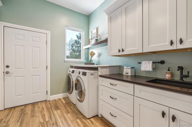 clothes washing area featuring cabinets, light wood-type flooring, washer and clothes dryer, and sink