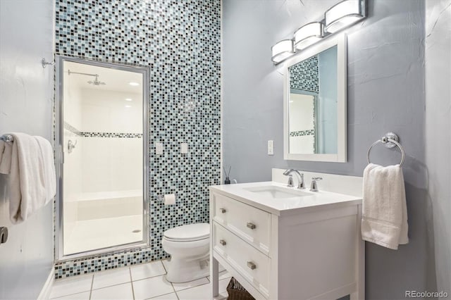 bathroom featuring a shower with door, vanity, tile patterned floors, toilet, and tile walls