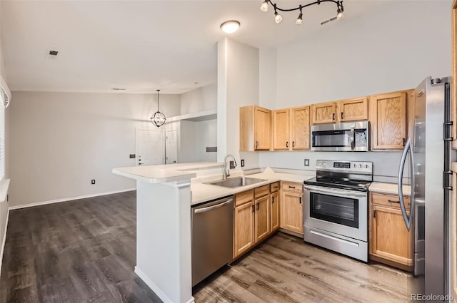 kitchen with sink, decorative light fixtures, appliances with stainless steel finishes, dark hardwood / wood-style flooring, and kitchen peninsula