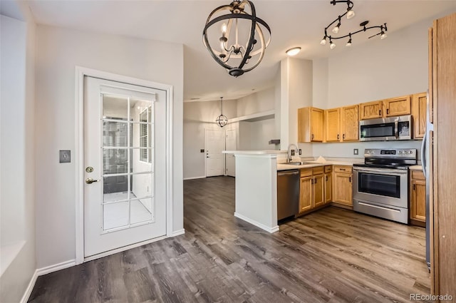 kitchen with appliances with stainless steel finishes, sink, hanging light fixtures, kitchen peninsula, and dark wood-type flooring