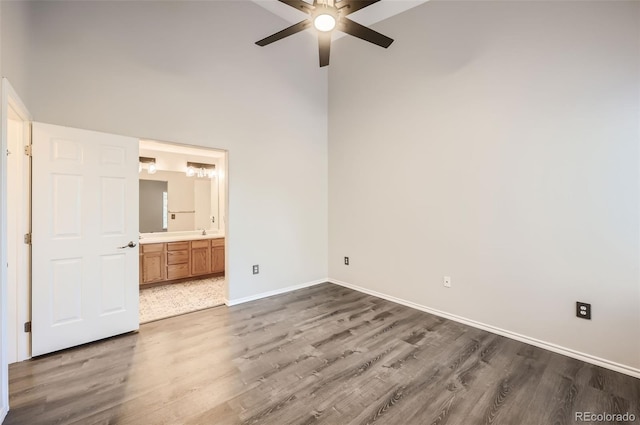 unfurnished bedroom featuring connected bathroom, a towering ceiling, dark wood-type flooring, and ceiling fan