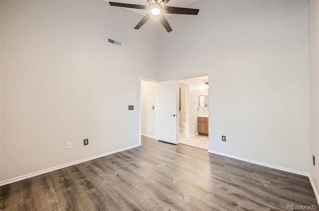 unfurnished bedroom featuring a high ceiling, ceiling fan, dark wood-type flooring, and ensuite bath