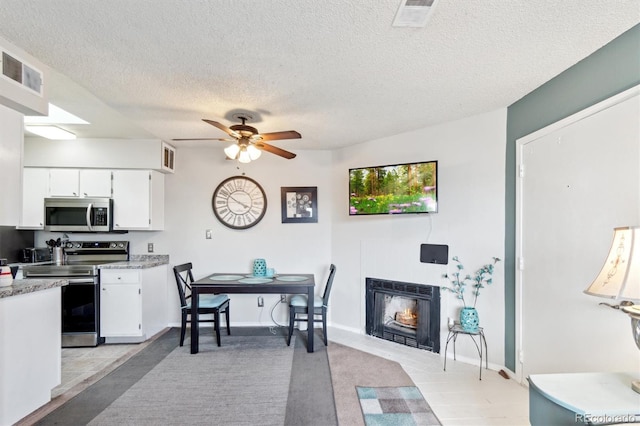 dining space with a lit fireplace, a textured ceiling, visible vents, and a ceiling fan