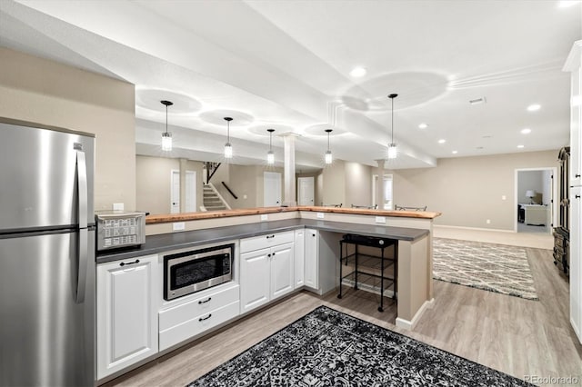 kitchen featuring kitchen peninsula, light wood-type flooring, stainless steel appliances, decorative light fixtures, and white cabinetry