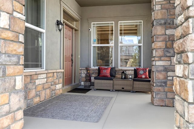 view of exterior entry with stucco siding, stone siding, and covered porch