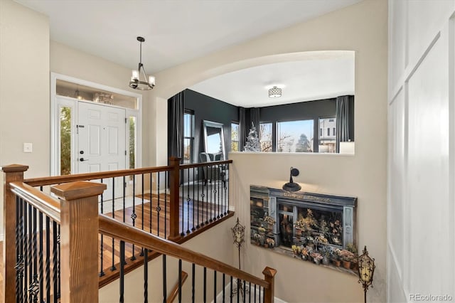 hallway featuring arched walkways, a notable chandelier, and an upstairs landing