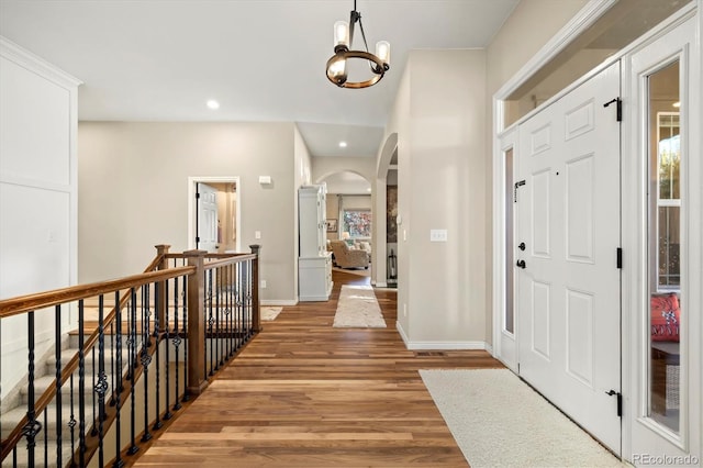 foyer entrance featuring recessed lighting, light wood finished floors, an inviting chandelier, arched walkways, and baseboards