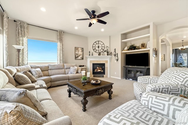 living room featuring ceiling fan, arched walkways, a tile fireplace, light colored carpet, and recessed lighting