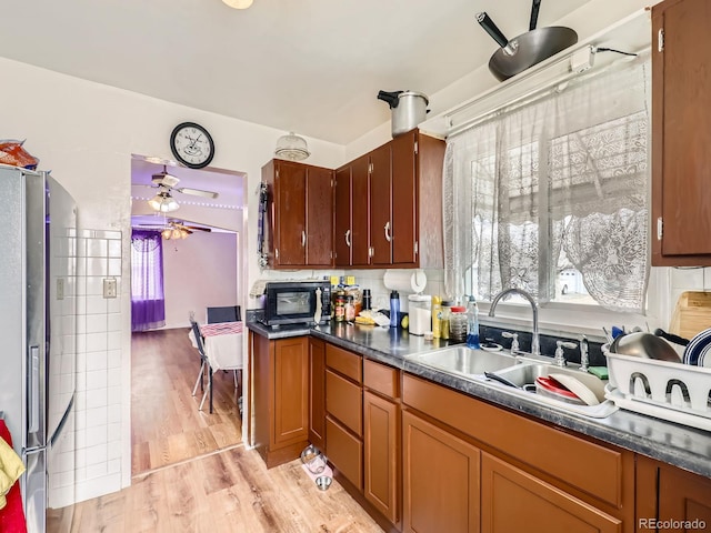 kitchen featuring sink, stainless steel refrigerator, ceiling fan, backsplash, and light hardwood / wood-style floors