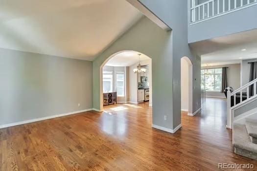 4630 Whitehall Ln, Highlands Ranch, CO 80126 - unfurnished living room with arched walkways, a chandelier, wood finished floors, high vaulted ceiling, and stairway