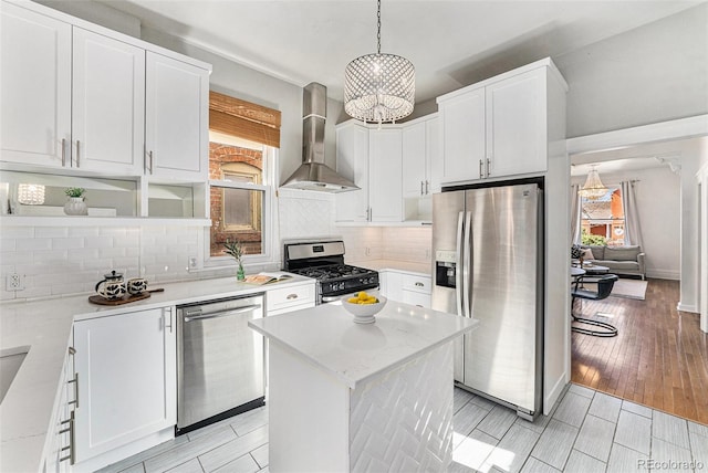 kitchen featuring a kitchen island, backsplash, stainless steel appliances, white cabinets, and wall chimney range hood