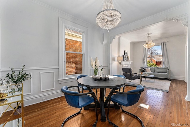 dining room featuring a chandelier, ornamental molding, wainscoting, a decorative wall, and wood-type flooring