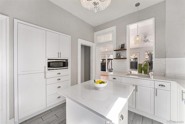 kitchen featuring a sink, stainless steel microwave, decorative backsplash, and white cabinetry