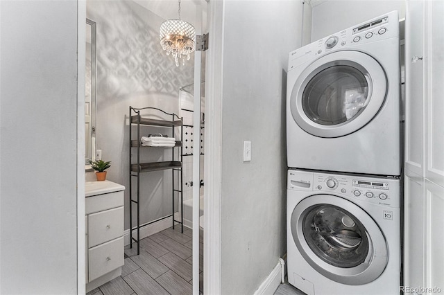 laundry area with wood finish floors, baseboards, stacked washer and dryer, laundry area, and an inviting chandelier