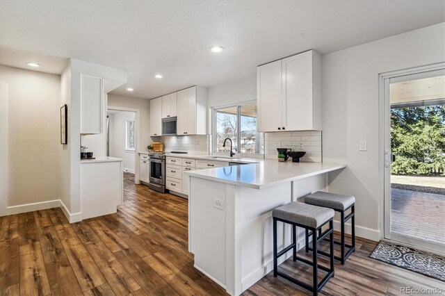 kitchen with backsplash, a kitchen bar, appliances with stainless steel finishes, dark wood-style floors, and white cabinetry