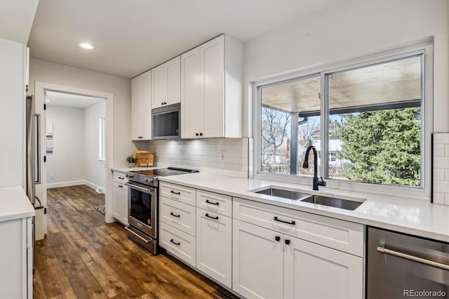 kitchen featuring light countertops, decorative backsplash, white cabinets, stainless steel appliances, and a sink