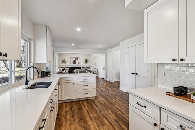 kitchen with open floor plan, decorative backsplash, a peninsula, white cabinets, and a sink